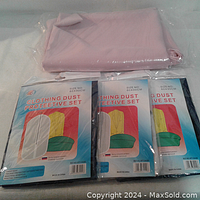 Three packed clothing dust protective covers laid side by side with a folded pink fabric tablecloth on top.