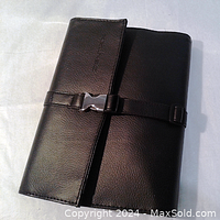 Closed view of black leather combo holder case with buckle closure showing textured leather and strap.