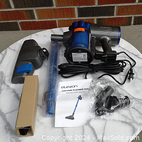 Photo showing vacuum components including main unit, metal wand, attachments in plastic bags, instruction manual, and power cord coiled.