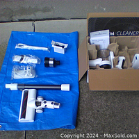 Vacuum cleaner components and accessories arranged on a blue tarp, includes main unit, wand, brush head, and smaller attachments.