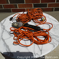 Long orange extension cord coiled with orange trouble light laid on round white marble surface outdoors.