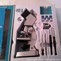 Top view of microscope set arranged in foam tray showing the microscope and various accessories including slides, reagent bottles, and tools.