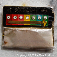 Social Battery pin in original packaging, showing enamel face with seven mood icons and slider.