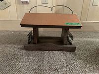 Front view of the wooden bird house with metal suet cages on both sides, sitting on a carpeted floor.