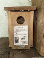 Close-up photo of the smaller WoodLink Woodpecker House showing front with round entrance hole and product label.
