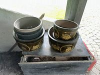 Photo shows a group of 6 pots including 3 brown pots decorated with yellow floral motifs and 3 plastic pots stacked inside each other.