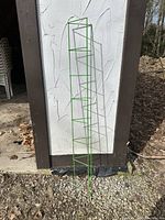 Single lime green metal garden ladder standing upright outside against a wall on gravel ground.