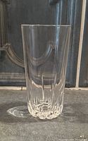 Tall clear glass with crinkly textured bottom visible, placed on a surface with a tiled wall background.