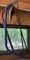 Two metal frame hand saws with attached blades, one blue (32 inches) and one red (34 inches) hanging indoors.