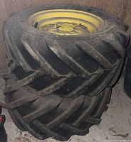 Two John Deere tires stacked indoors with yellow rims and dirt on treads.