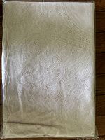 Folded white lace tablecloth with intricate swirly pattern shown in detail.