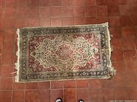 Full view of the small Persian beige and red rug with a central medallion pattern and floral designs on a red background with a beige center and dark borders.