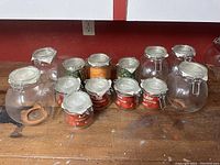 Thirteen glass storage jars of various sizes arranged on wooden surface, showing airtight hinged lids with metal clasps.