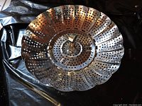 Photo showing metal expandable perforated steamer strainer basket