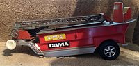 Side view of the red and blue fire truck toy showing the extendable ladder and GAMA logo