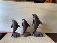 Front view of the three hardwood dolphin sculptures of varying sizes on a wood surface with a wooden backdrop.