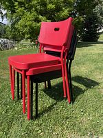 Four stackable IKEA chairs, two red and two black, sitting on grass outdoors showing condition and color.