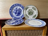 Four vintage collectible ceramic plates displayed on a wooden surface, two blue and white and two green and white designs, showing overall lot contents.