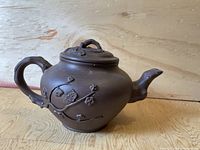 Side view of brown Chinese Yixing teapot showing floral branch detail and lid with handle.