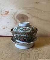 Side view of bowl with lid and saucer stacked, showing floral and panel decorations