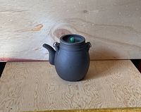 Full front view of the dark egg-shaped Yixing teapot showing the spout, handle, and green lid knob.
