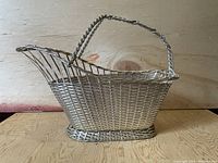 Side view of hand made metal woven wine holder basket showing elongated oval shape and braided wire handle.