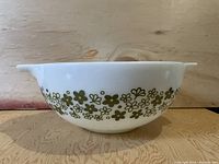 Side view of white CorningWare Pyrex bowl featuring a green floral pattern band around its sides on a wooden surface.