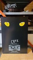 Full view of framed poster with yellow cat eyes on black background and "CATS" and production info in white text.