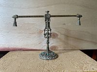 Front view of silver-plated brass jewelry stand with intricate decorative details and horizontal bar with tassels