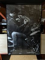 Full view of the vintage Harley-Davidson poster showing the couple embracing next to the motorcycle in a black and white photograph.