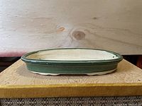 Top and side view of oval bonsai pot showing green glazed exterior and beige base on wooden surface.
