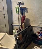 Wooden barrel holding multiple cleaning mops, gloves on mop handles, O-Cedar mop bucket partially visible, plastic pet gate leaning against barrel
