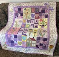 Front view of handmade quilt with assorted patchwork patterns and pastel colors draped on a sofa.