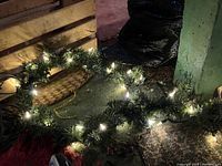 Close-up of the lighted green pine-like garland with warm white LED lights turned on, showing greenery texture and attached lights.
