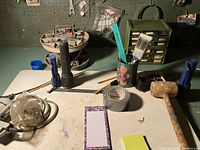Workbench surface showing wooden mallet, duct tape, brush, and pencil holder with tools