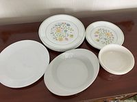 Stack of dinner plates including 7 patterned with floral design, 1 plain white, luncheon plates with floral pattern, and 3 bowls.
