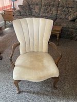 Front view of wooden Queen Anne style chair with cream/beige plush velvety upholstery, scalloped vertical channel tufted backrest, wooden arms and legs.