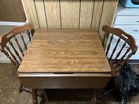 Top view of the wooden dropleaf kitchen table with two chairs pushed in at the sides, showing the table surface and wood grain finish.