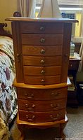Front view of wooden jewelry armoire stacked on wooden hamper showing drawer and knob details