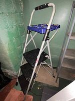 Front view of Werner 3-step steel step stool with tool tray in basement, showing black plastic steps, blue tray, and steel frame.