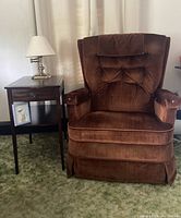 Photo showing brown Lazy Boy recliner rocker chair next to vintage wooden end table with drawer and lower shelf holding framed bird print, with beige curtains in background.