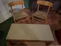 Two Danish Mid-Century Modern J39 Folkestole chairs with woven seats and wooden backs next to a rectangular beige canvas top folding table with wooden legs.