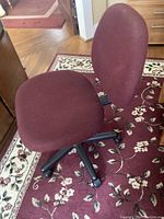 Front angle view of the maroon fabric office chair on a floral area rug, showing cushioned seat and backrest with black five-wheel base.