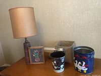 Wide view of two lamps, two metal containers, cloth bin, and floral wall hanging on table
