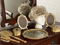 Full view of the 1940s celluloid vanity set on dresser with tray, hairbrush, mirror, two photo frames, two boxes, and the platinum wig on mannequin head.
