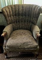 Front angle view of the vintage taupe fanback chair showing the floral pattern upholstery, padded arms, and carved wooden claw feet.
