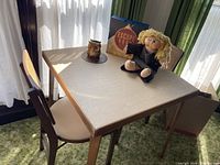 Vintage Stakmore folding card table and two cane-backed chairs, with ceramic owl napkin holder, Egypt themed escape room game, and Cabbage Patch Kid doll on top.