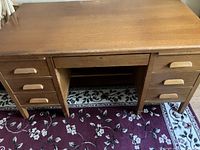 Front view of wooden desk showing six side drawers and central pull-out shelf, smooth top surface with minor wear.