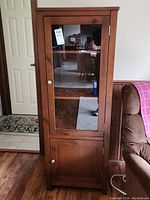Front view of wood cabinet with glass upper door and solid lower door, visibly labelled with tag.