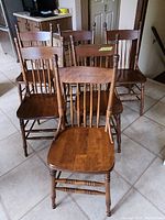 Front view of six wooden chairs grouped together showing their spindle backs and turned legs.
